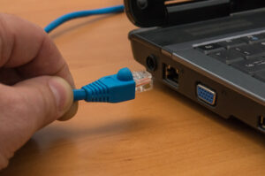 Hand plugging a blue RJ45 Ethernet cable into a laptop network port to run an NBN speed test.